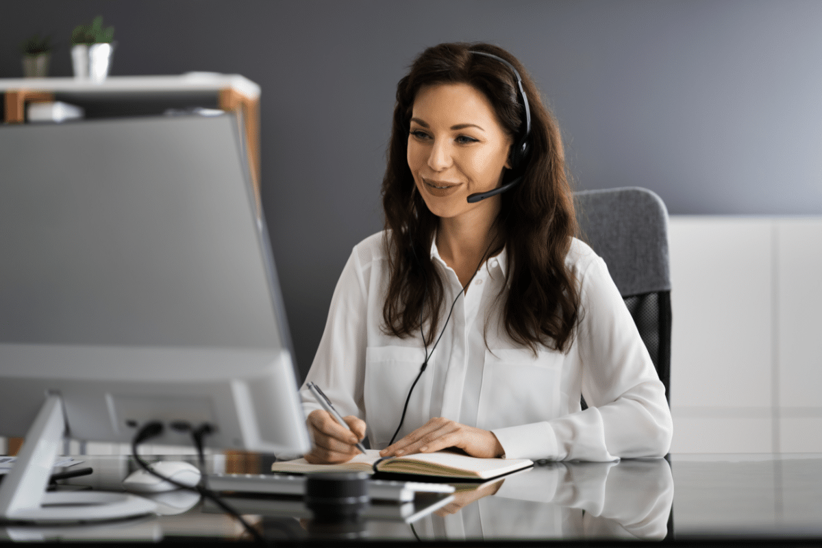 A woman with a headset sitting at a desk with a computer.